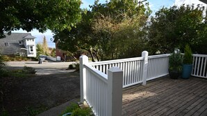 A wooden deck with white railings, surrounded by greenery and a pathway leading to a house. - Charming 2-bedroom house in downtown Langley. (Langley)