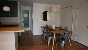 A modern kitchen with wooden countertops, a dining area with a wooden table and metal chairs, and a hallway leading to a door. - Charming 2-bedroom house in downtown Langley. (Langley)