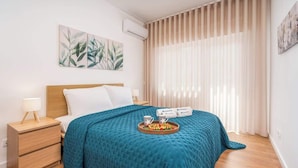 A modern hotel room with a bed, a nightstand, a tray with breakfast items, and a window with curtains. - Bright & Spacious Flat w/ Balcony by Host Wise (Portimão)