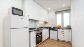 A modern kitchen with white cabinetry, a built-in oven, a microwave, and a window providing natural light. - Bright & Spacious Flat w/ Balcony by Host Wise (Portimão)