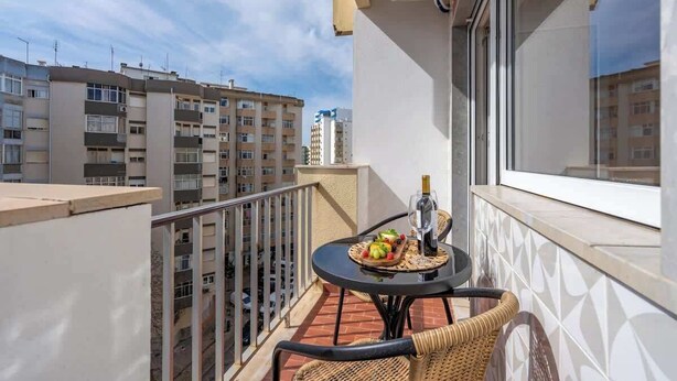 A balcony with a table, wicker chairs, and a bottle of wine. - Bright & Spacious Flat w/ Balcony by Host Wise (Portimão)