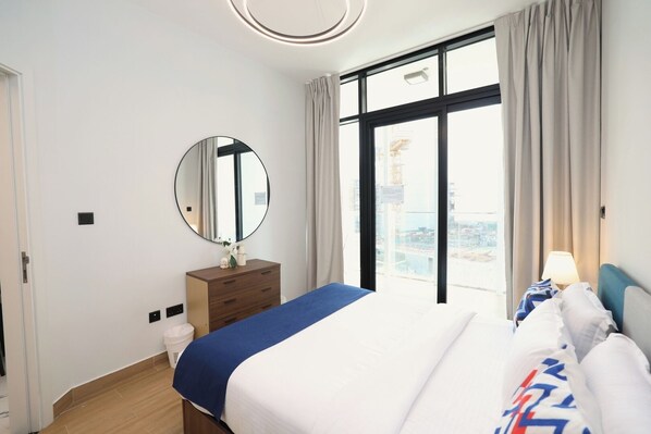 Une chambre d’hôtel avec un lit, une commode, un miroir, une fenêtre donnant sur un paysage agréable et une lampe.