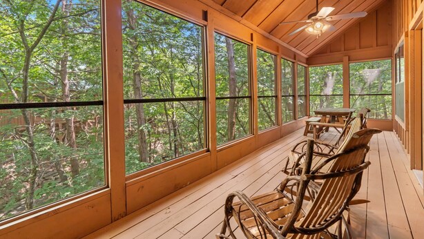 A wooden deck with large windows, wooden furniture, and a ceiling fan. - Family Cabin, Resort Access, Near Entertainment! (Branson)