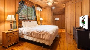 A wooden-paneled bedroom with a bed, two bedside lamps, a ceiling fan, and a dresser. - Family Cabin, Resort Access, Near Entertainment! (Branson)