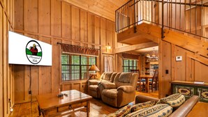 A wooden interior with a sofa, armchair, and table. A sign with a logo and text is visible on the wall. - Family Cabin, Resort Access, Near Entertainment! (Branson)