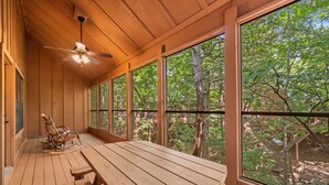 A wooden deck with a table and chairs, large windows offering a view of trees, and a ceiling fan. - Family Cabin, Resort Access, Near Entertainment! (Branson)