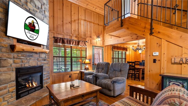 Un acogedor interior de cabaña con chimenea de piedra, un sofá cómodo, un sillón mullido y un comedor con muebles de madera.