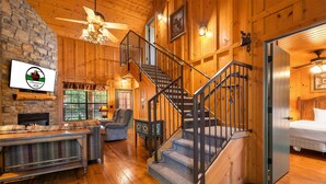 Un interior de madera con chimenea, una escalera y una cama.