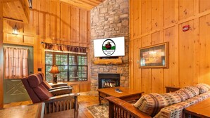 A cozy cabin interior with a stone fireplace, wooden furniture, and a television mounted on the wall. - Your Branson Hideaway | 2 King Beds, Pool & Scenic Views (Branson)