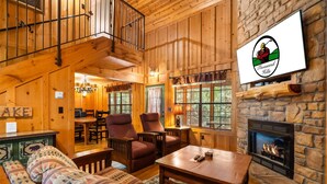 A cozy log cabin interior with a fireplace, wooden furniture, and a dining area. - Your Branson Hideaway | 2 King Beds, Pool & Scenic Views (Branson)