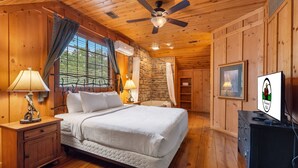 Ein gemütliches Schlafzimmer in einer Holzhütte, mit einem Bett, Nachttischen, einem Deckenventilator und einer Steinwand.