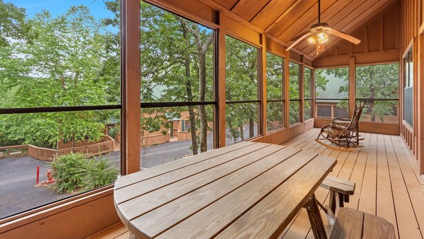 Eine Holzdar Terrasse mit Tisch und Stühlen, große Fenster mit Blick auf Bäume und eine Straße.