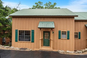 A wooden building with a green door, windows with shutters, and a metal roof.
