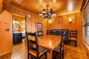 A wooden interior with a dining table and chairs, a chandelier, and a kitchen area.