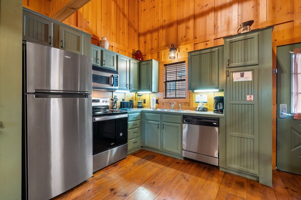 A kitchen with wooden walls, stainless steel appliances, and light green cabinets.