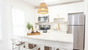 A modern kitchen with white cabinetry, stainless steel appliances, and a central island with bar stools. - CrestNest- Modern 2BD, 1BA - 2.5 Blocks to Beach (Wildwood)