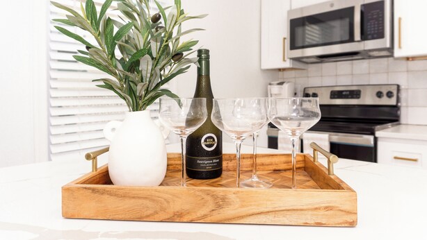 A kitchen with white cabinets, a microwave, and a wine bottle on a wooden tray. - CrestNest- Modern 2BD, 1BA - 2.5 Blocks to Beach (Wildwood)