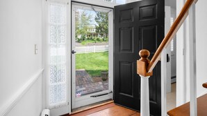 Une porte noire avec une balustrade en bois, un chambranle de porte blanc et une porte vitrée ornée de rideaux en dentelle.