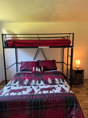 A bunk bed with a red and black plaid bedspread, a wooden nightstand with a lamp, and a white wall. - 4-bed Cabin- ATV/UTV trail access from the driveway with a bar/covered patio (Crivitz)
