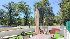 Ein Terrassenbereich im Freien mit Tisch und Stühlen, umgeben von einer niedrigen Mauer und viel Grün.