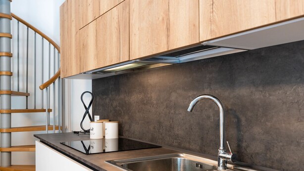 Eine moderne Küche mit Spülbecken aus Edelstahl, Holzschränken und einer Wendeltreppe.