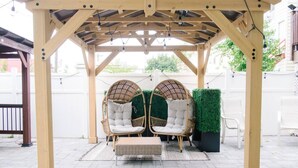 A wooden pergola with two wicker chairs and a small table, surrounded by a paved patio. - `The Hideaway` Modern Apartment w/Sauna and Grill (Troy)
