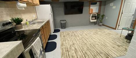 Una cocina moderna con armarios de madera, un microondas negro, una estufa y un lavamanos. Hay una alfombra grande en el suelo y un cubo de basura pequeño en la esquina.