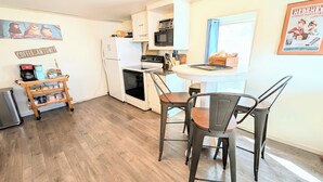 A compact kitchen with a refrigerator, oven, microwave, and a small dining area with metal chairs. - Hershey Music Box 2 - Duplex near HersheyPark, Giant Center, Hershey, Palmyra (Hummelstown)