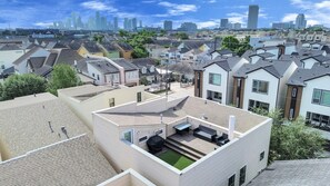 A residential area with modern houses, a rooftop with outdoor seating, and a city skyline in the background. - Stylish Heights Home w/ 4BR, 3.5BA + Office Spaces / Perfect for Long-Term Stays (Houston)
