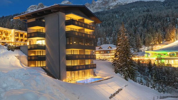 A modern hotel with multiple floors, snow-covered surroundings, and a mountain backdrop. - Alma Alpina Lodge (Nova Ponente)