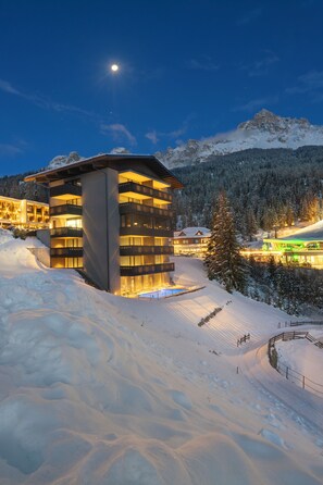 A modern hotel with multiple floors, snow-covered surroundings, and a mountain backdrop.