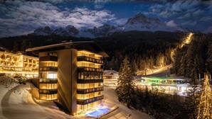 A modern hotel with multiple floors, a pool, and a ski slope in the background. - Alma Alpina Lodge (Nova Ponente)