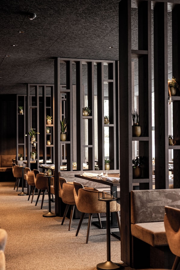A modern restaurant interior with high wooden partitions, seating arrangements, and potted plants.