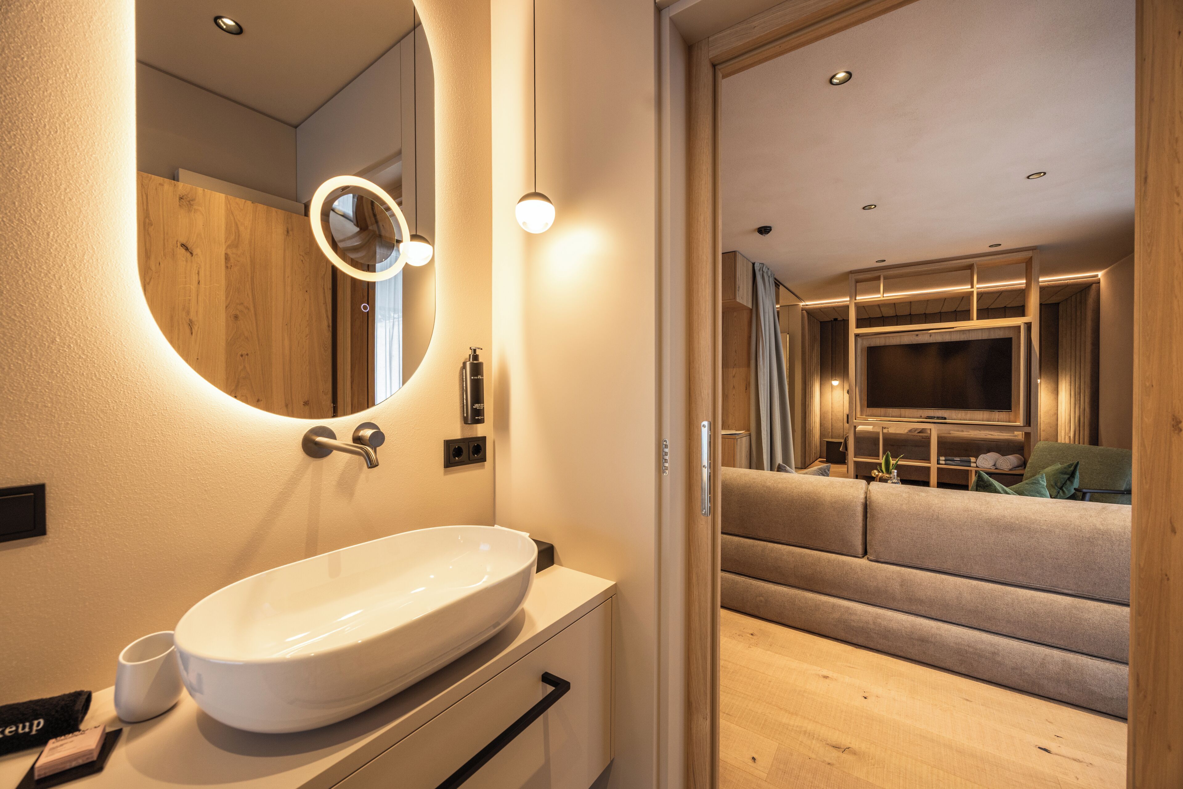 A modern bathroom with a large oval sink, a mirror with a circular light, and a wooden vanity.