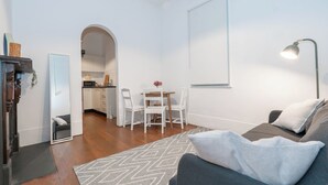 Un salon moderne avec un canapé gris, un tapis à motifs et un coin repas comprenant des chaises blanches et une table.