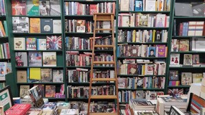 Une librairie avec de nombreuses étagères remplies de livres, une échelle et quelques livres exposés sur des tables.