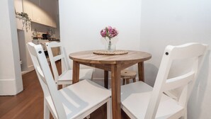 Un coin repas avec une table ronde en bois, des chaises blanches et un vase rempli de fleurs.