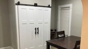 Un coin repas avec une table et des chaises, une armoire blanche et une fenêtre avec des stores.