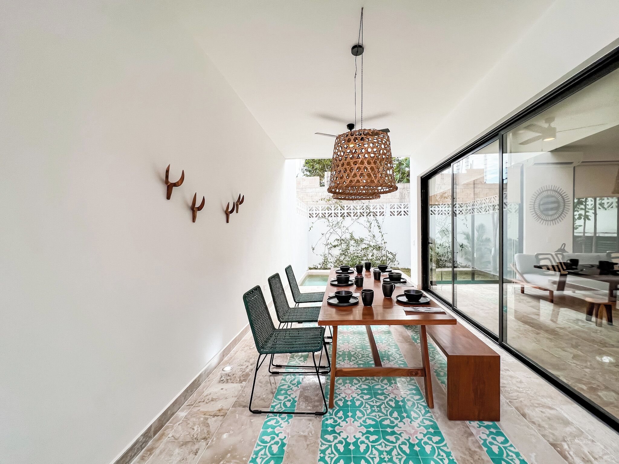 A modern dining area with a wooden table, green chairs, and a patterned rug.