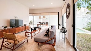 A modern living room with a flat-screen TV, wooden furniture, a large window, and a view of the outdoors.