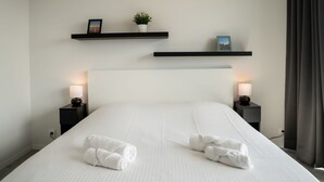 A hotel room with a large bed, two bedside tables with lamps, a headboard, and two wall-mounted shelves with decorative items. - Lovely apartment for 5 people with WIFI, TV and balcony (Bruges)
