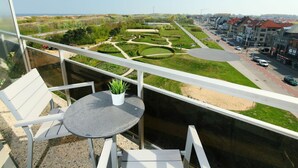 A balcony with a table and chairs, overlooking a landscaped garden and a street with buildings. - Lovely apartment for 5 people with WIFI, TV and balcony (Bruges)