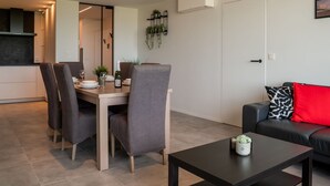 A modern living room with a dining area, a black leather sofa with a red cushion, and a small table with a plant. - Lovely apartment for 5 people with WIFI, TV and balcony (Bruges)