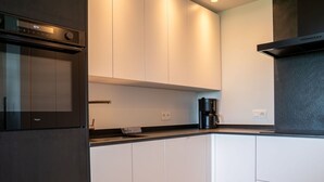 A modern kitchen with white cabinetry, a black countertop, and a built-in oven. - Lovely apartment for 5 people with WIFI, TV and balcony (Bruges)