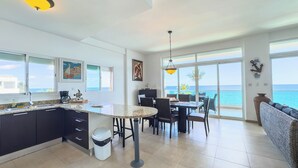 A modern kitchen with a dining area, large windows, and a view of the sea.