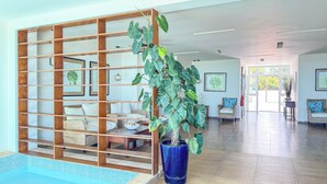 A spacious lobby with a wooden partition, wicker furniture, a large potted plant, and a tiled floor.