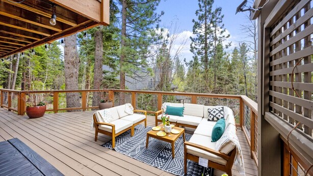 Eine Holzterrasse mit einer Couch und einem Couchtisch, umgeben von Bäumen.