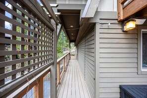 A covered outdoor deck with a wooden railing, a light fixture, and a view of the surrounding area.