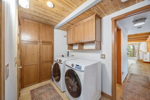Un cuarto de lavandería con dos lavadoras, armarios de madera y un techo de vigas de madera.