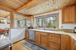 A modern kitchen with wooden cabinets, granite countertops, and a large window offering a view of trees.